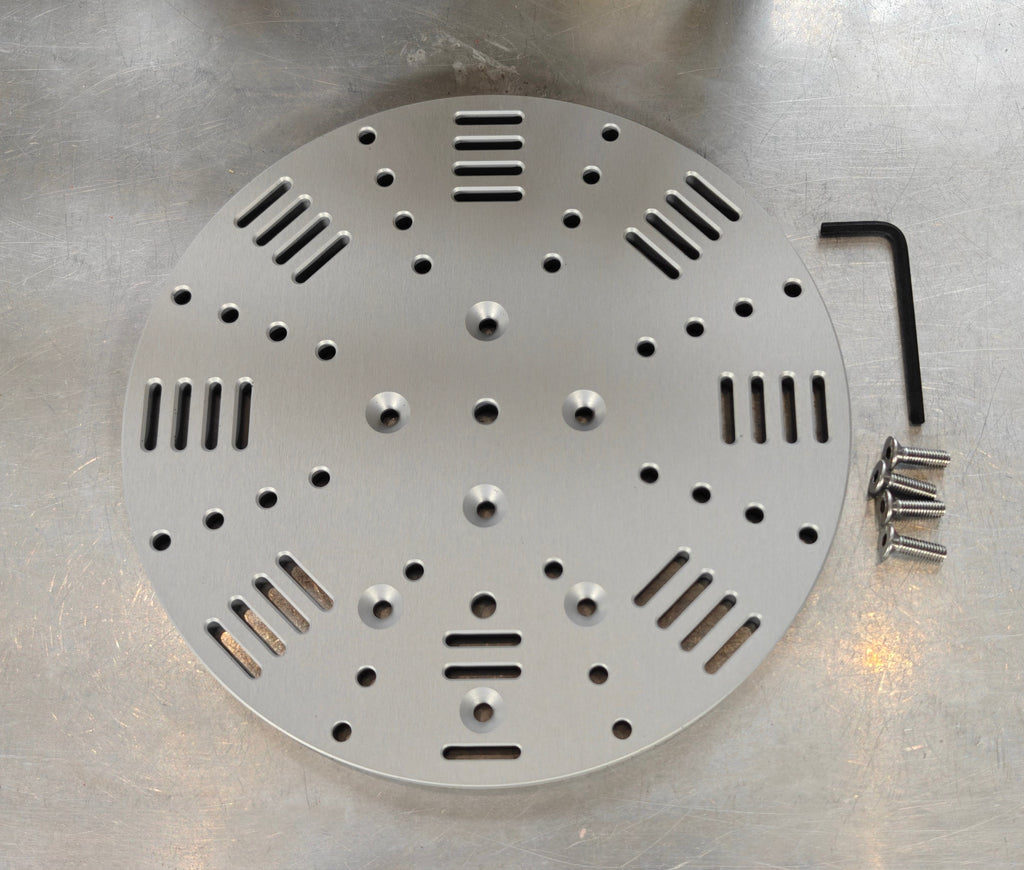 A round silver aluminium mounting plate, with milled slots for straps and mounting holes. With fixing screws and hex key.